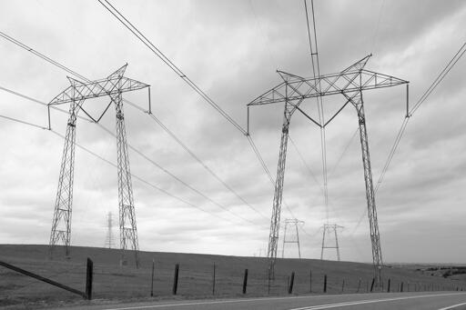 A pair of high-voltage power transmission line "portal" style pylons in a field along a road. Other pylons are visible in the background.