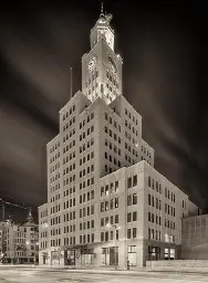 An early 20th century office building, with setbacks and a clock tower, at night.