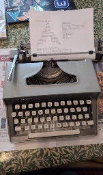 A photo of my typewriter, a Remington Travel-Riter Deluxe with a sheet of A4 paper in it, on which I have manually typed the output of fastfetch and ping. The typewriter is apparently running Arch Linux with linux-hardened. My shell is sh. It has no CPU, no GPU, and zero bytes of RAM. The ping command was going to 9.9.9.9. All packets were returned with decent speed.