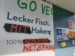 Fischstäbchen Werbeplakat von Frosta. Der Slogan "Lecker Fisch. Ohne Haken. 100% frei von Zusätzen." wurde teilweise mit Graffiti überschrieben zu: "Lecker Fisch. Mit Haken: 100% Schleppnetzfang."

Darüber in grüner Schrift: "Go vegan"