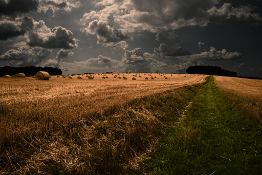 Daylight photo.
Scattered haystacks and clouds being shy above the endless country lane.