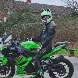 Samantha sitting on a Kawsaki Ninja 500 SE 2024 with a Black Racing Suit, Green and White Cat Eared Helmet on.