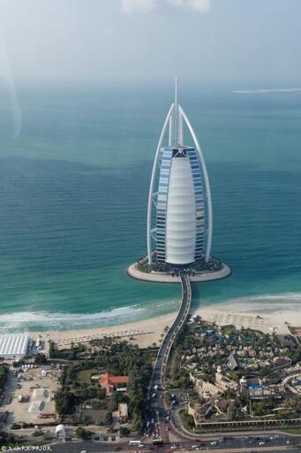 A photograph taken about 15 years ago when approaching Dubai's Burj al Arab by helicopter. The small island that the hotel sits on appears to be floating and tethered to the land by the private road bridge that gently snakes from the main road. Near the top of the hotel, above the triangular sail structure of the hotel, is the circular helicopter platform that is our destination.