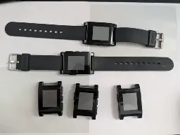 Five original Pebble watches on a desktop. Two of them have original straps, the other three have no straps.
