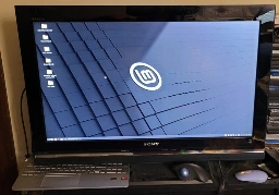 The image shows an older flat screen TV with the keyboard from a laptop tucked under it and a trackball mouse in front. 