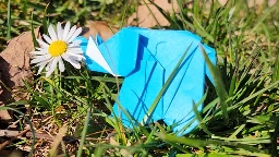 an origami elephant, in the grass, smelling a daisy